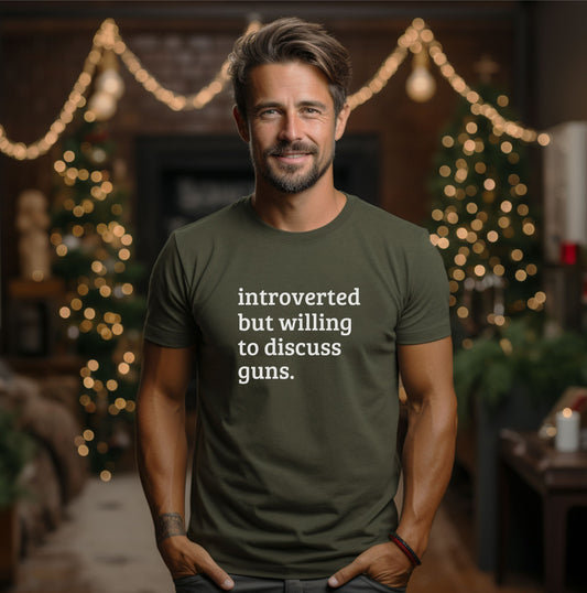 Men wearing a military green t-shirt saying in front on the shirt, white imprint: Introverted But Willing to Discuss Guns 